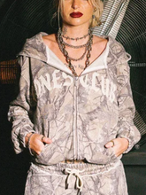 Front close-up of model wearing treecamo zip-up hoodie with Bones Club lettering and layered jewelry