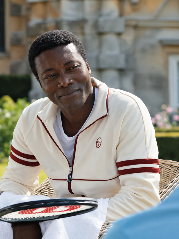 Benjamin Clementine wearing the cream track jacket from The Gentlemen season 2 with burgundy stripe sleeves